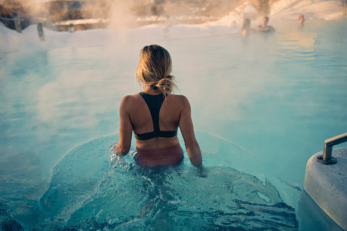 Woman walking into a steamy pool in the winter at a Scandinavian style spa.