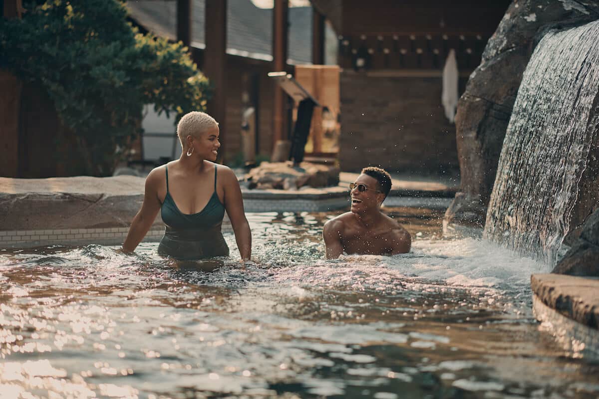 Two people in a waterfall pool at Nordik Spa Nature in Quebec.