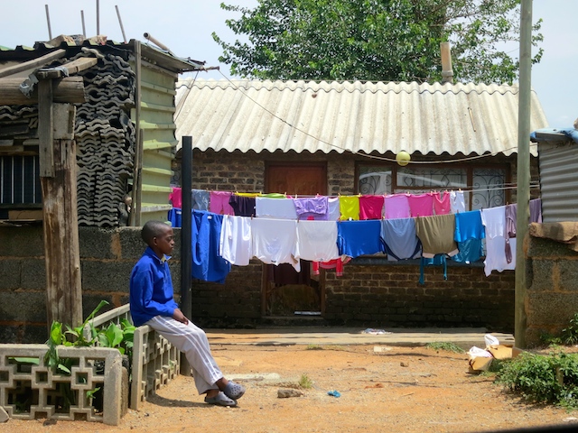 Boy in a blue shirt in Soweto with colourful laundry behind.