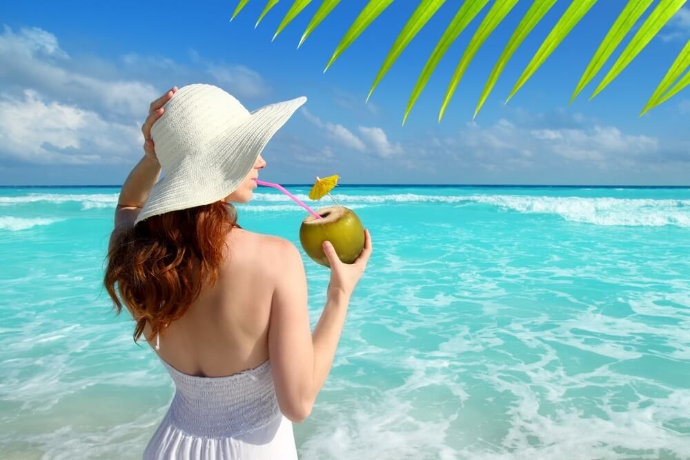 woman drinking coconut on a turquoise tropical beach