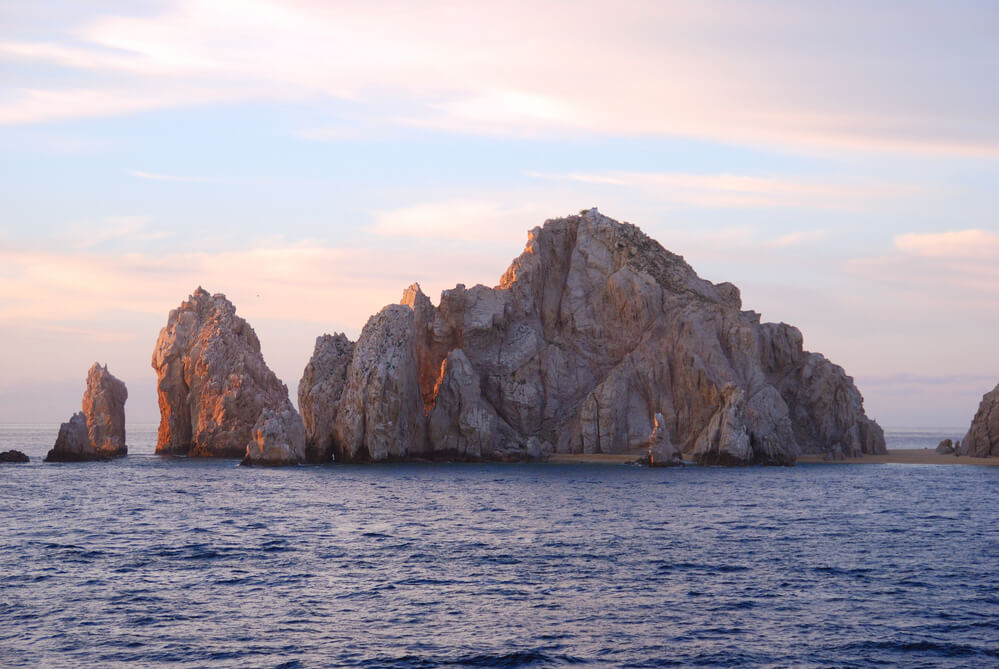 rocks on the water in los cabos at a pink sunset