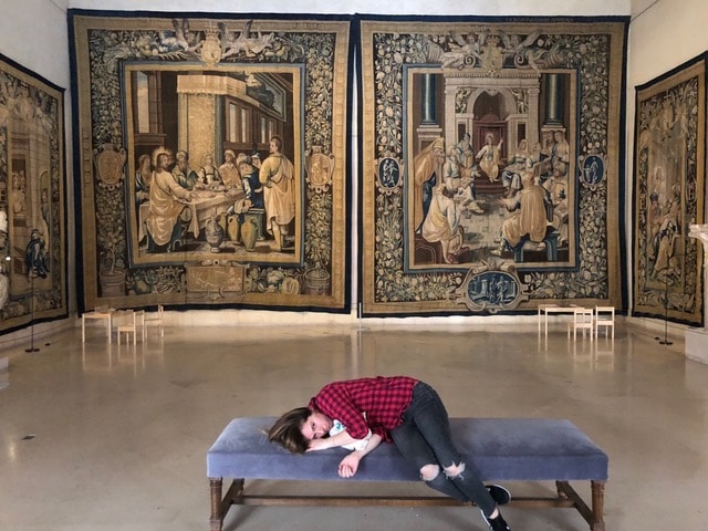 Girl lying on bench in Paris museum with tapestries