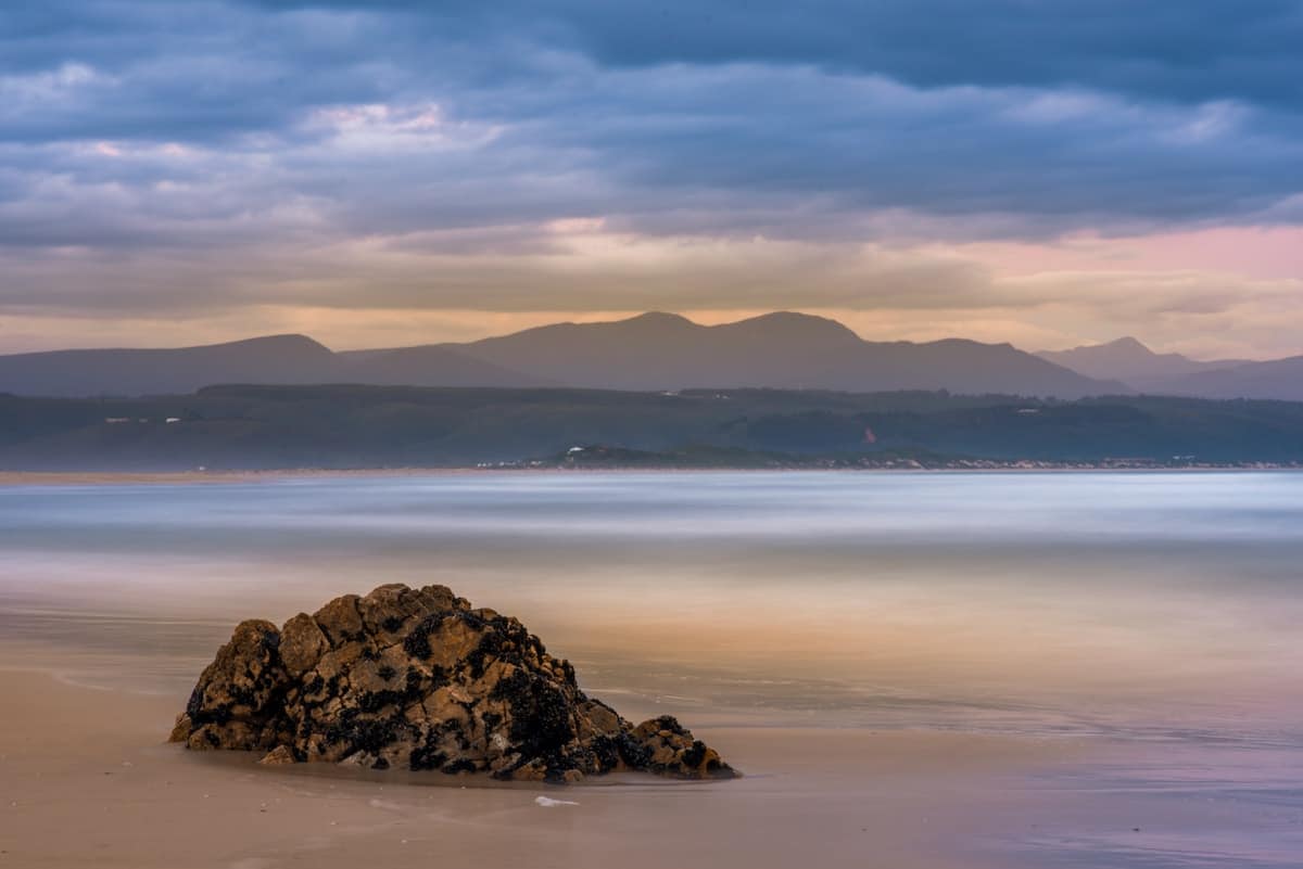 pastel beach shot of plettenberg bay with big boulder