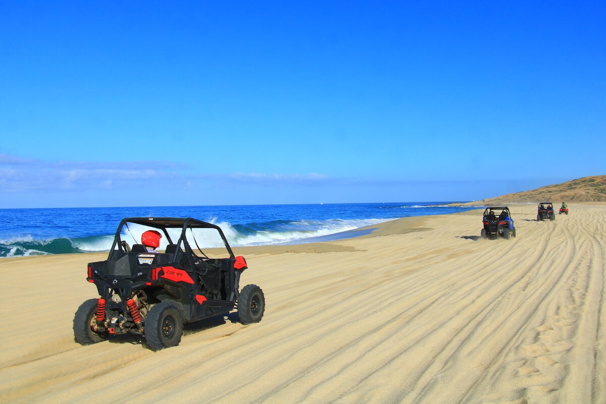 3 utvs and an atv riding in the sand at Migrino Beach in Cabo San Lucas Mexico
