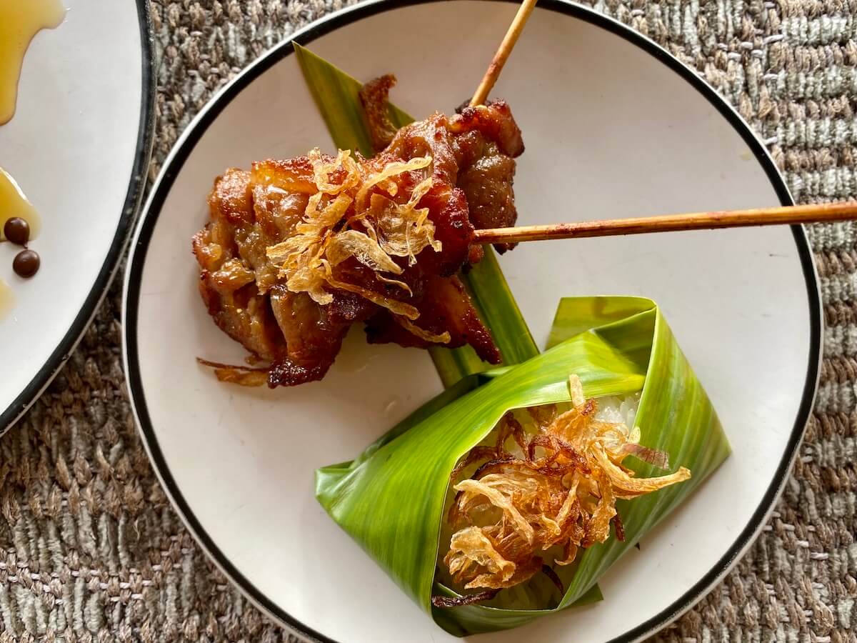 Plate with upscale Thai market food of pork on a skewer and rice in banana leaf