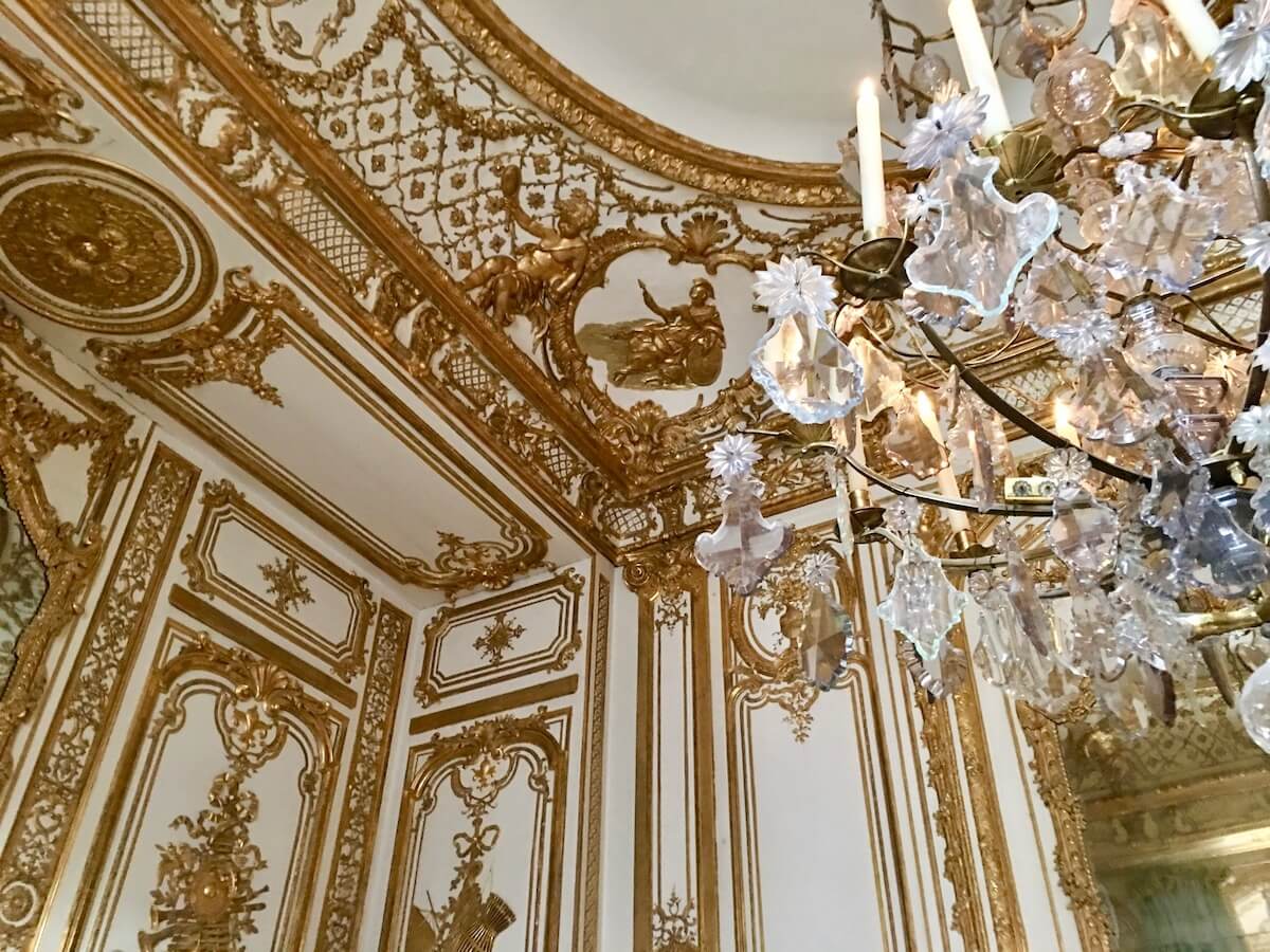 Ornate gilt and cream walls with a chandelier at the Chateau de Versailles